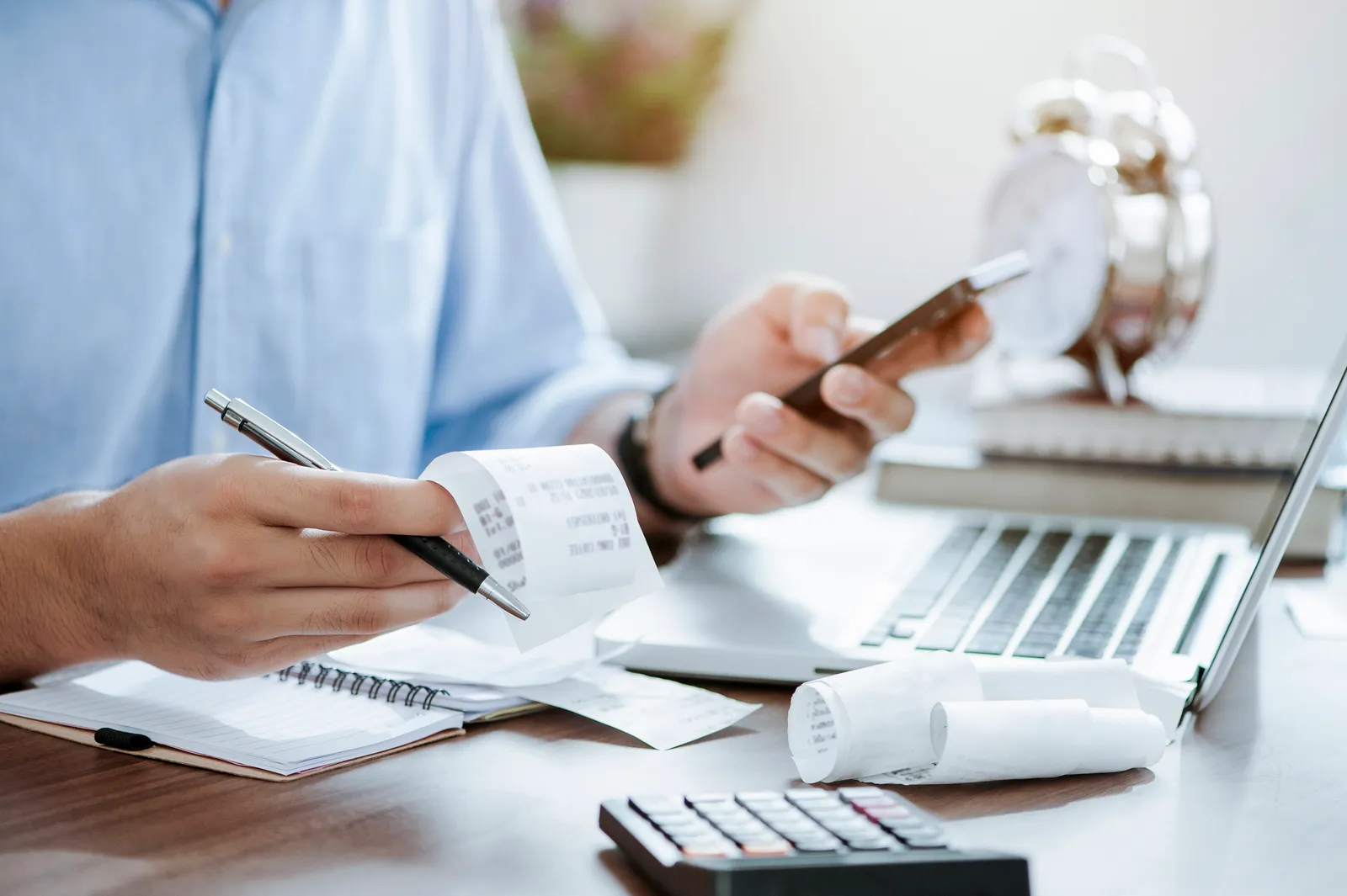 Escritorio de trabajo con recibos, calculadora y despertador junto al portátil