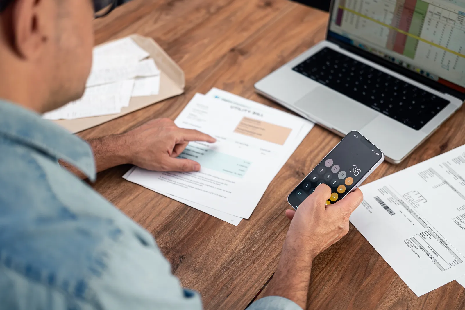 Empresario sumando facturas con la calculadora del móvil sobre el escritorio